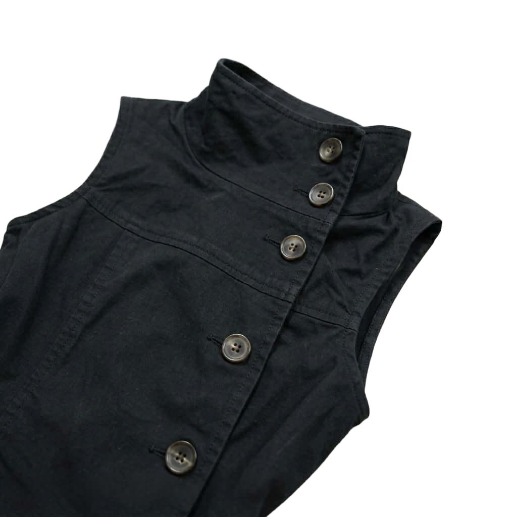 Structured Black Sleeveless Vest Top - High Neck Structured Black Sleeveless Vest Top - High Neck This black sleeveless vest features a structured stand collar and a sophisticated side-button closure for a unique, asymmetrical look. Designed with a tailor