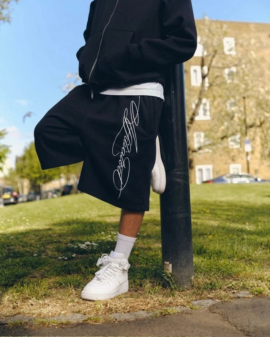 Person wearing oversized streetwear shorts with cursive signature design, showcasing modern streetwear style.