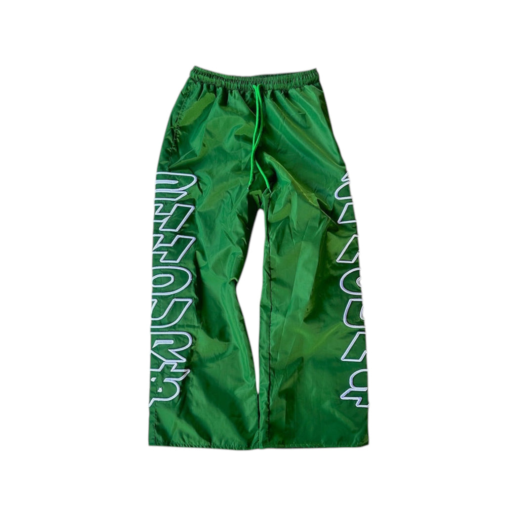 Y2K nylon track pants in shiny green fabric with bold text design, showcasing a baggy streetwear style.
